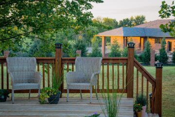 A gray wooden deck with two woven chairs and potted plants.