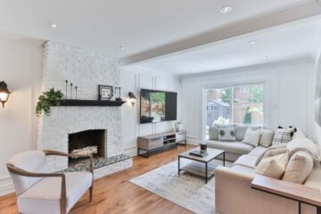 A white living room with hardwood floors, light gray furniture and a white brick fireplace.
