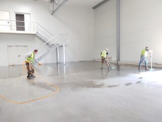 Three people wearing yellow safety vests are cleaning the floor using a hose and two mops.