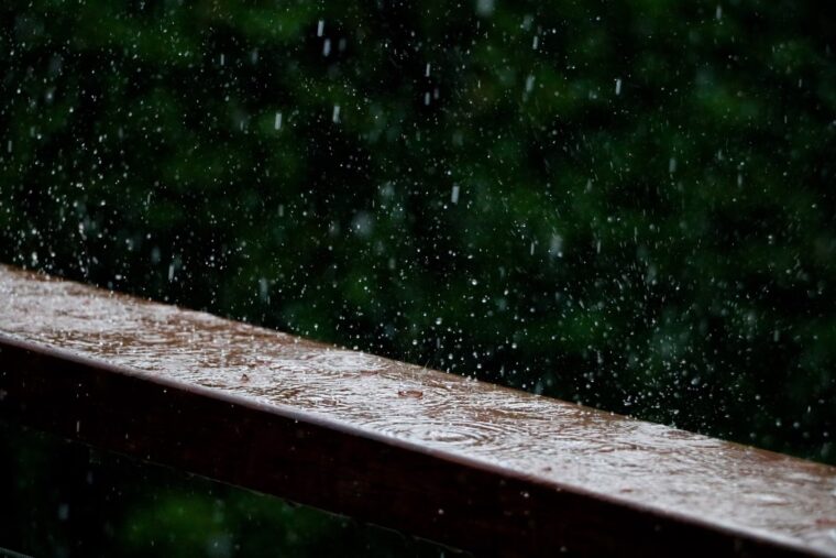 Raindrops bouncing off a wooden deck railing.
