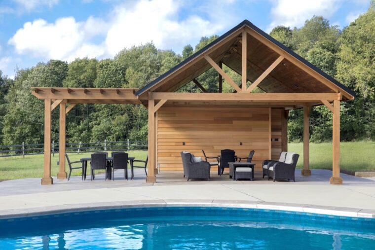 A gray pool deck with a wooden awning and black patio furniture.