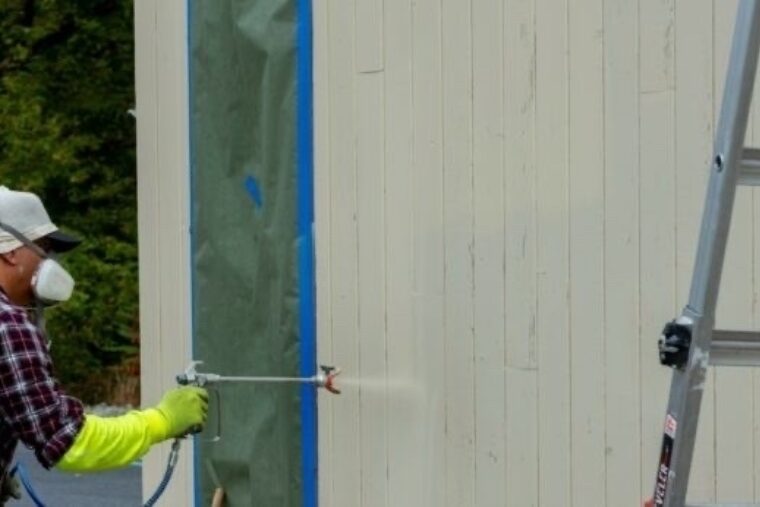 A person applying ZAR® Deck & Siding Solid Color Coating on a white wall constructed with T1-11 plywood siding.