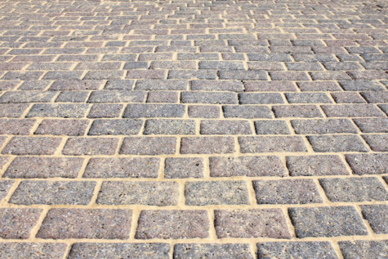 A sidewalk paved with grayish-red brick and tan mortar.