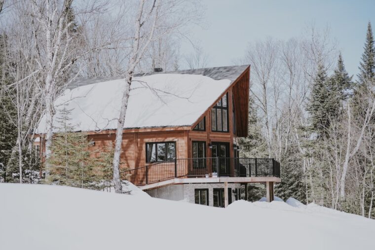 A three-story home with wooden siding. The yard is covered in snow and surrounded by pine trees.