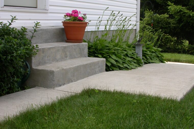 Three steps are leading up to a house door. There is a concrete sidewalk that leads around the house.