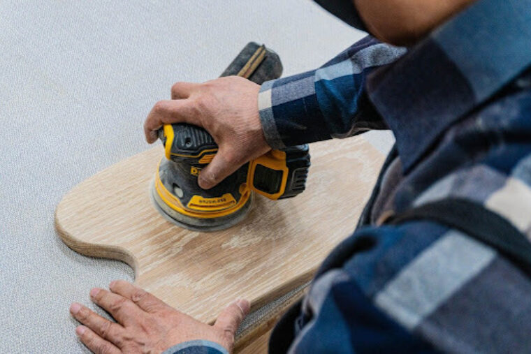 A person wearing a blue flannel is sanding a piece of wood.