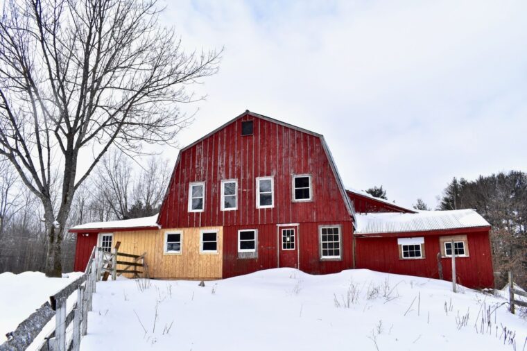 A barn on a hill covered in snow with red T1-11 plywood siding.