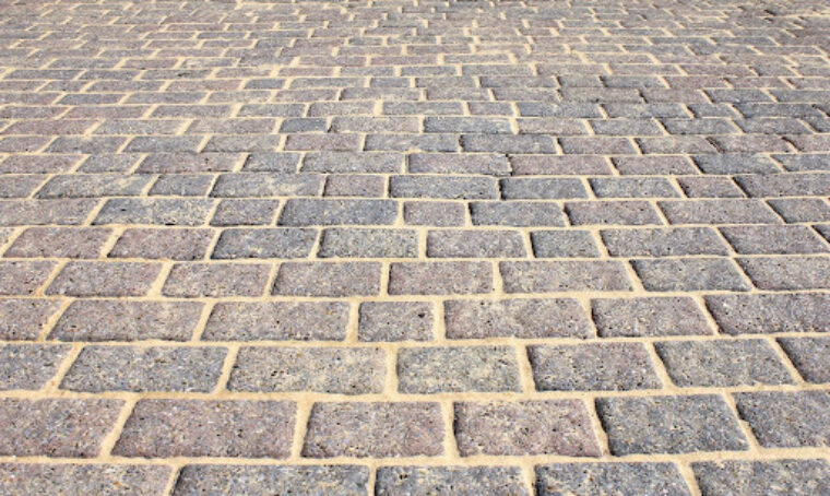 A sidewalk paved with grayish-red brick and tan mortar.