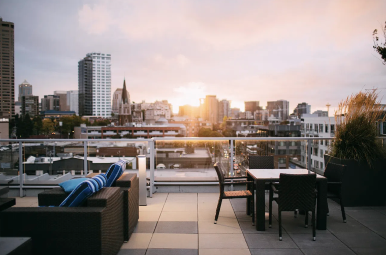 The picture depicts a rooftop outlook over a city. On the deck, there are two areas for seating.