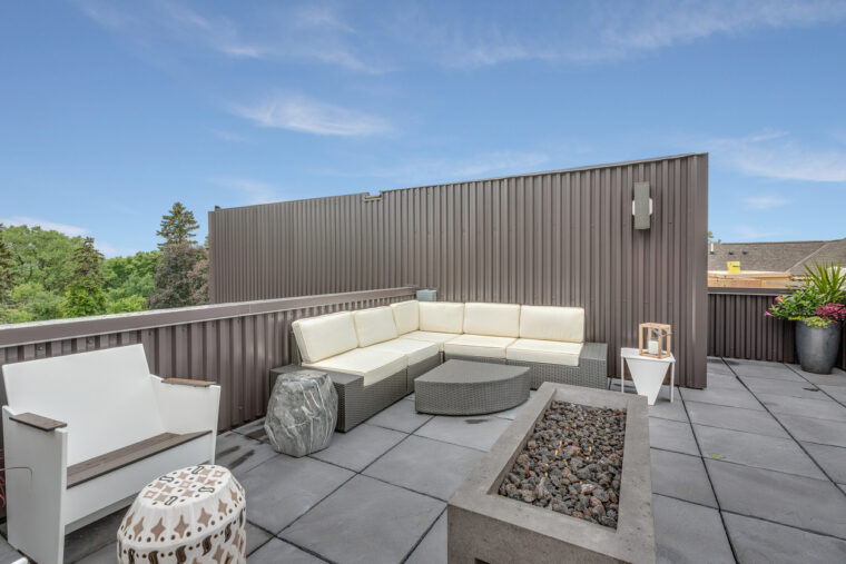 The picture depicts a gray rooftop with a fireplace, seating areas and small tables.